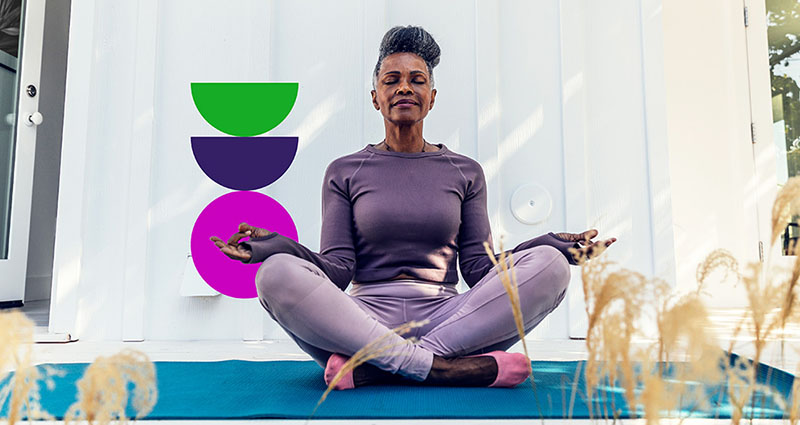  A woman is sitting cross-legged in a meditative pose outdoors, with her eyes closed and a calm expression. Abstract colorful shapes are displayed beside her.