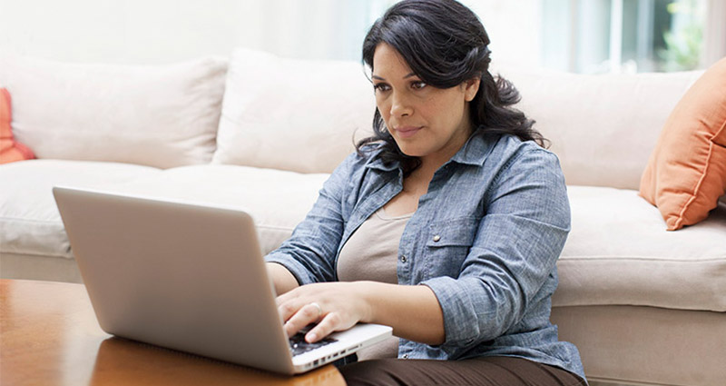 A woman sitting on the floor in her living room, focused on her laptop while working or browsing online.