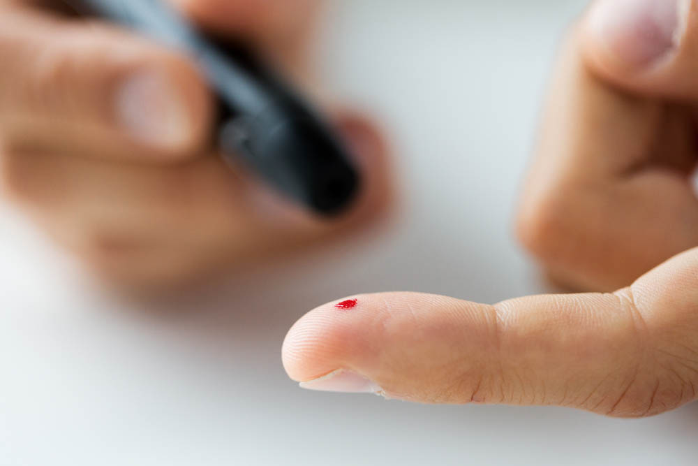 Close-up of a person pricking their fingertip with a lancet, showing a drop of blood, during a blood sugar test.