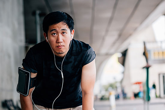 Man with earphones and armband taking a break outdoors, under an overpass, looking upward.