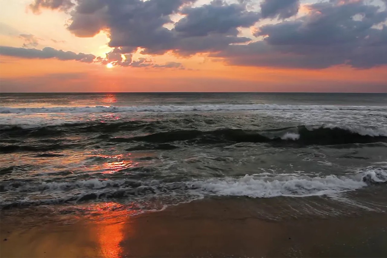 Waves crashing on the shore at sunset with colorful clouds in the sky