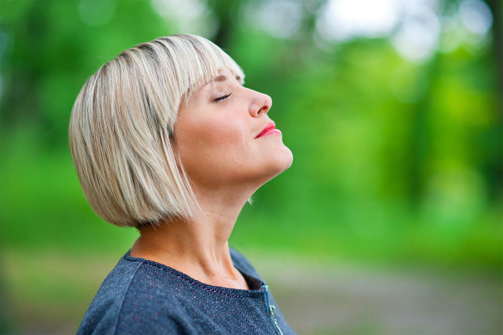 Blonde woman taking a deep breath in a green outdoor setting