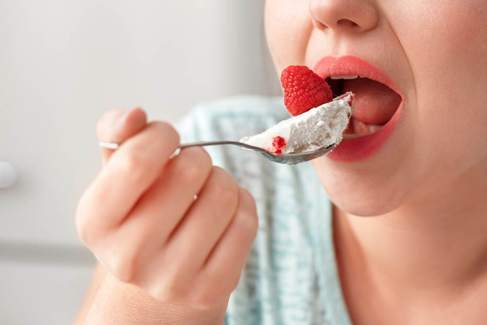 Young woman sitting at table in kitchen holding teaspoon eating cake breaking diet mouth close-up
