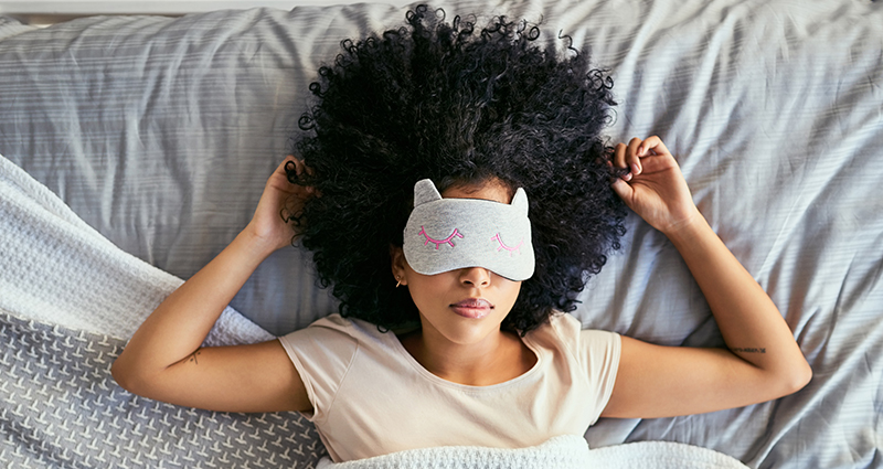 Woman sleeping with a sleep mask on, lying in bed.