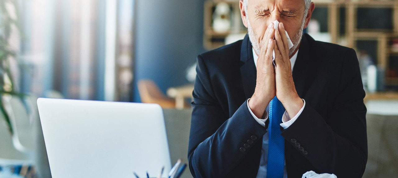 Man in a suit with nasal congestion blowing his nose in the office.