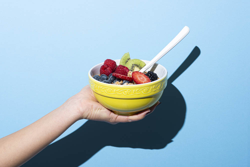 Womanr's hand holding Bowl with muesli chocolate, nuts and berries on blue background.Studio shot