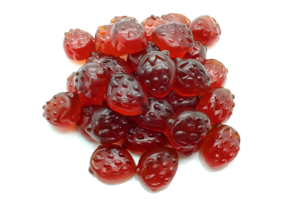 A pile of red, strawberry-shaped gummy candies arranged on a plain white background.