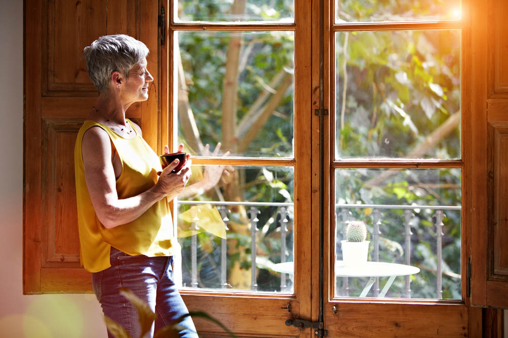 Shot of a mature woman standing by a window at home drinking a cup of coffee