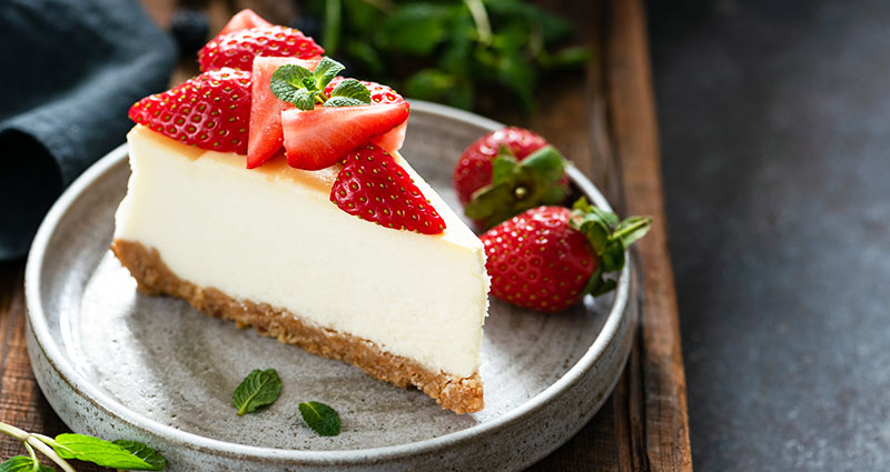 A plate with a slice of cheesecake. The cheesecake is topped and garnished with freshly sliced strawberries