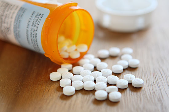Prescription bottle tipped over with white pills scattered on a wooden surface.