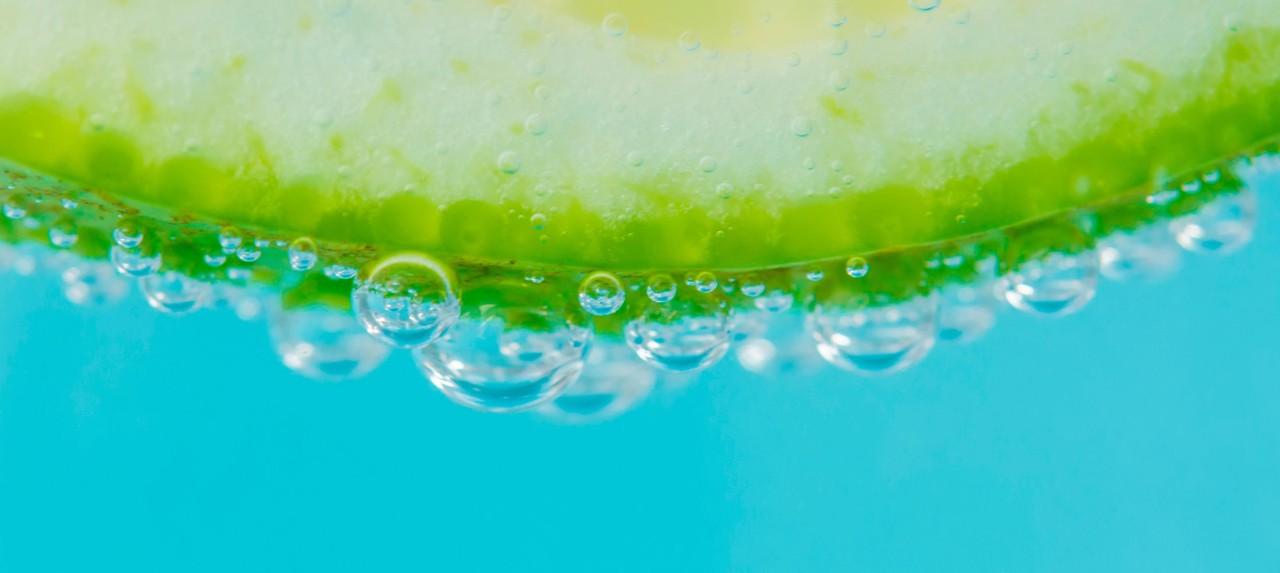 : A close-up view of a slice of green apple submerged in sparkling water, with bubbles forming around the edge