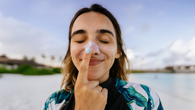 A young woman applying sunscreen to her nose while smiling playfully