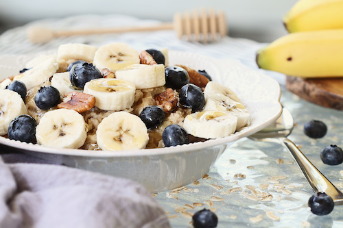 Hot breakfast of healthy oatmeal with pecans, bananas, blueberries and honey over a rustic background. Image shot from overhead.