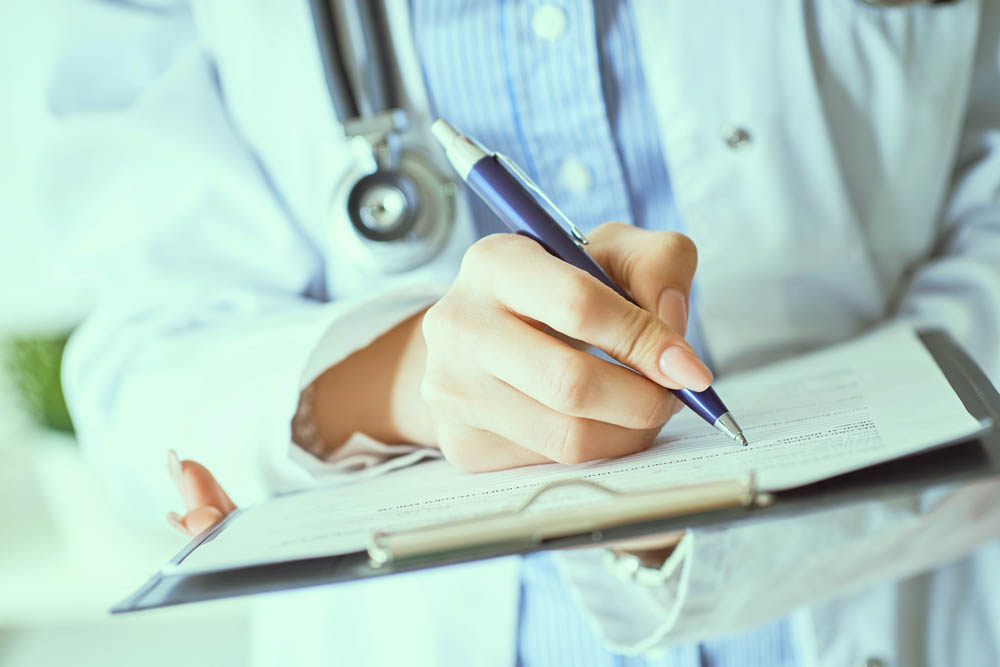 Female doctor hand hold silver pen filling patient history list at clipboard pad.