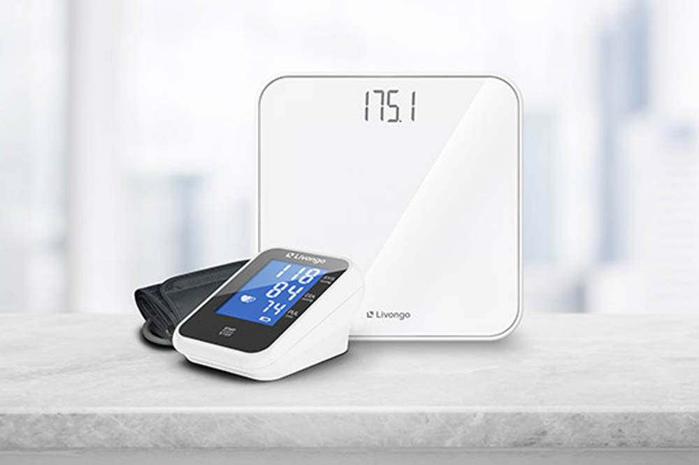 Digital blood pressure monitor and white smart scale on a marble surface against a blurred background.
