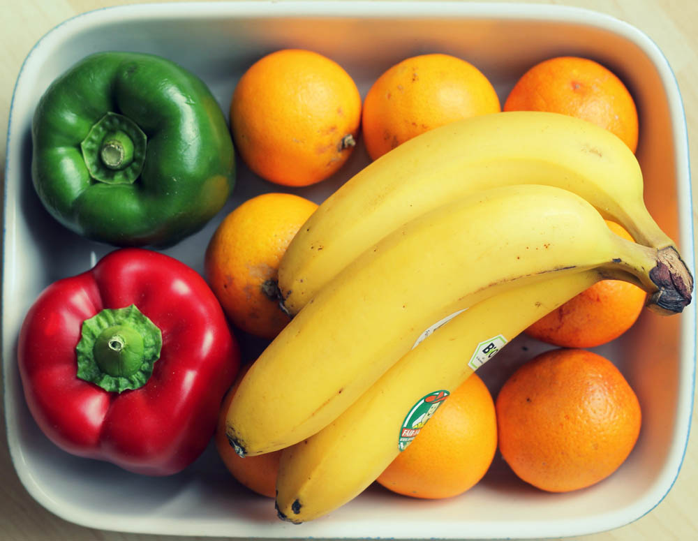 A white rectangular dish with bananas, oranges, a green bell pepper, and a red bell pepper.