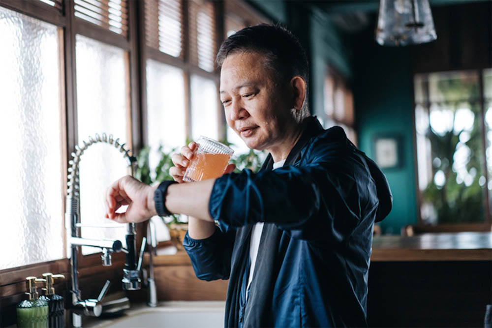 A person in a modern kitchen drinking a healthy beverage while checking their smartwatch.