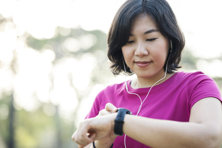 Woman outdoors wearing earphones and checking her fitness tracker.