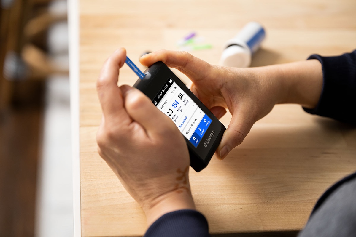 Person checking glucose levels with a glucometer at a wooden table.