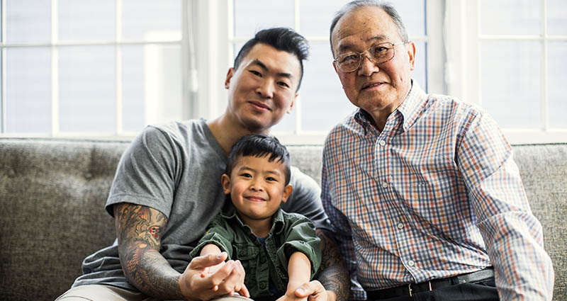 Three generations of a family sitting together on a couch, smiling at the camera.