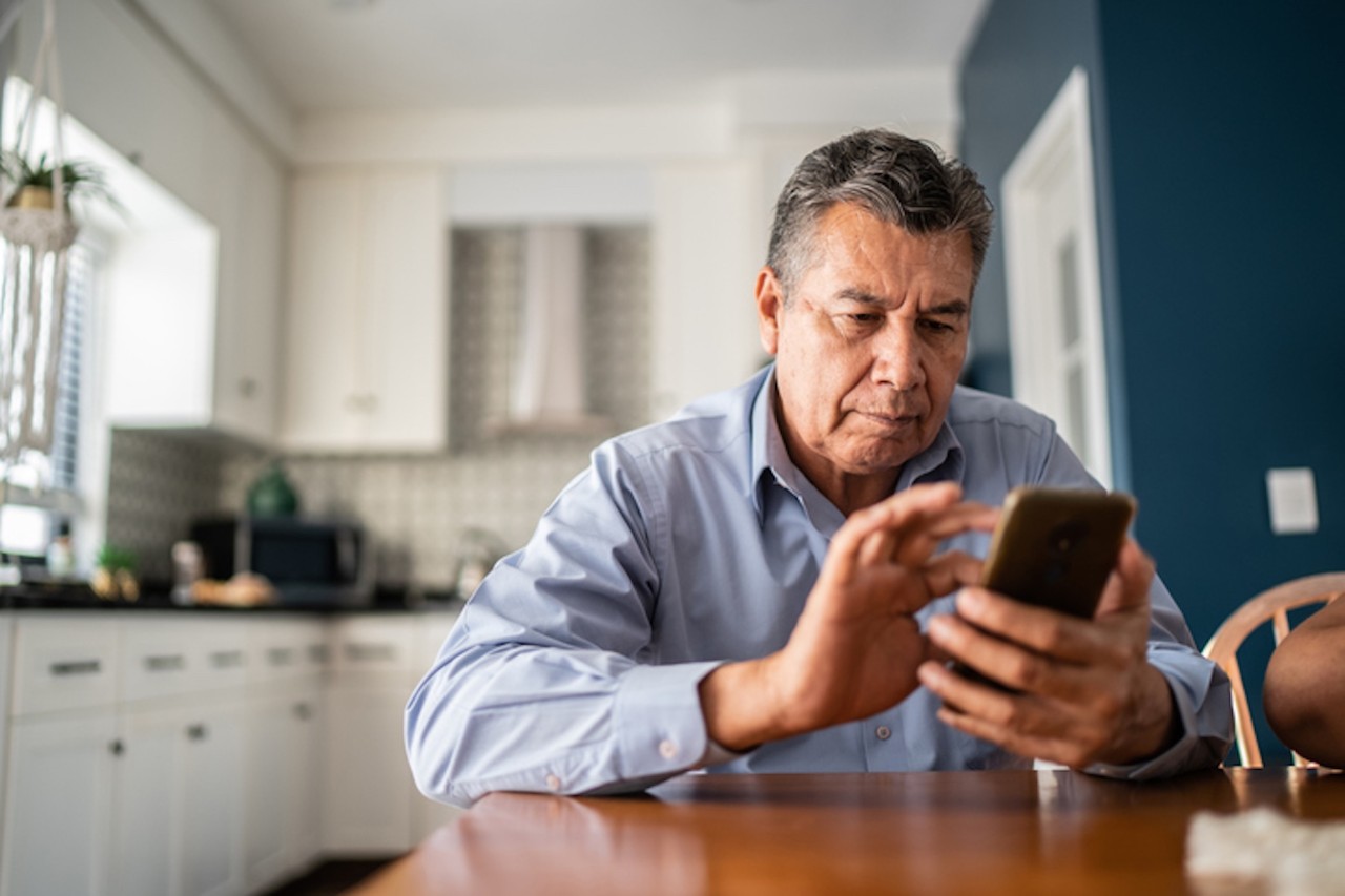 Serious older man sitting at a table using a smartphone