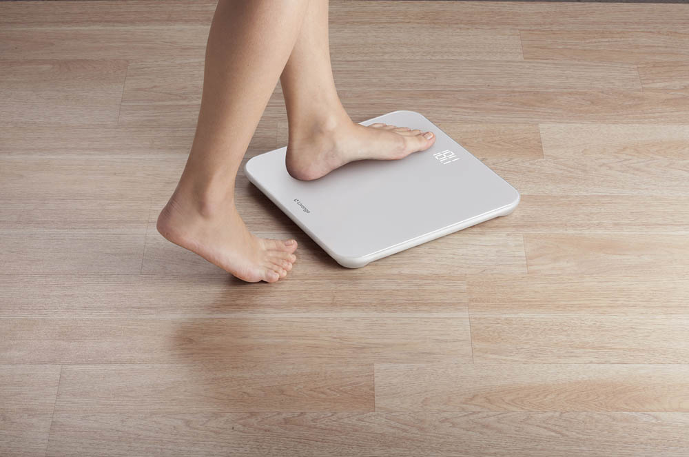 A person stepping onto a white digital bathroom scale on a wooden floor.