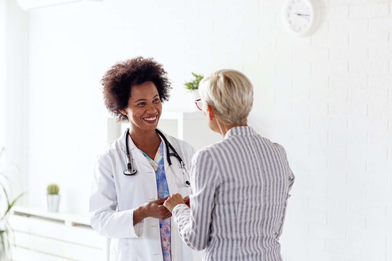 A doctor in a white coat smiling while shaking hands with a patient in a bright, modern medical office.