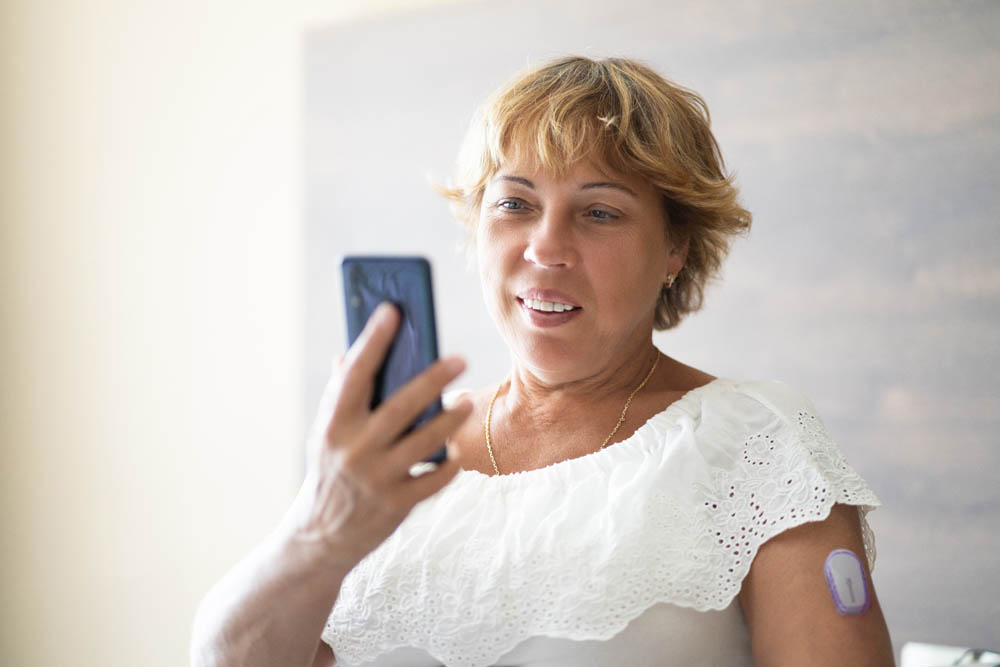 Woman Testing Glucose Level With Continuous Glucose Monitor On Mobile Phone