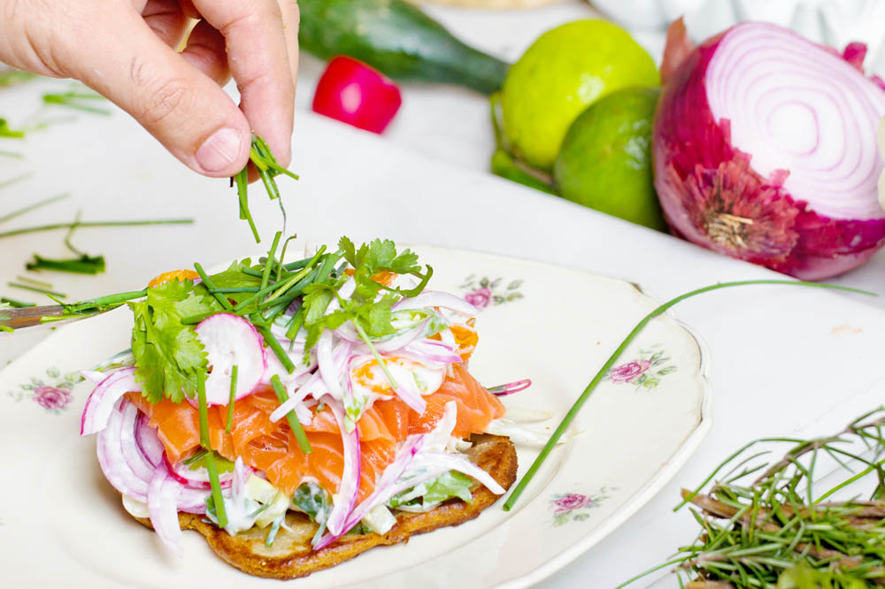 A hand adding fresh herbs to a colorful dish topped with vegetables, with various ingredients visible in the background.