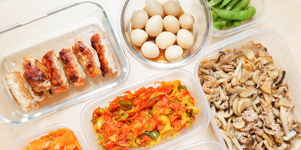 Assorted meal prep containers with grilled chicken, quail eggs, edamame, and mixed vegetable stir-fry.