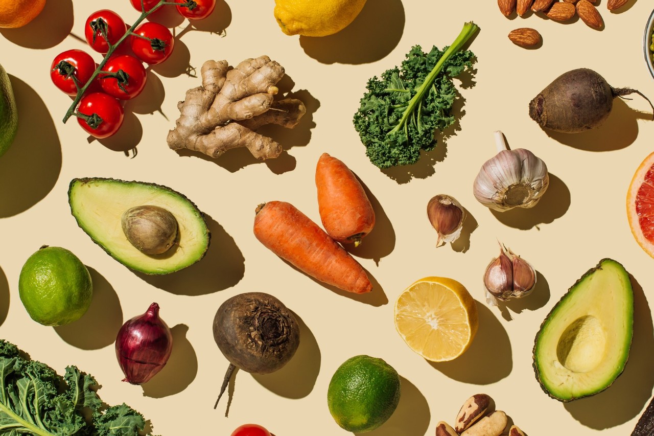 Assortment of fresh fruits, vegetables, and nuts on a beige background.