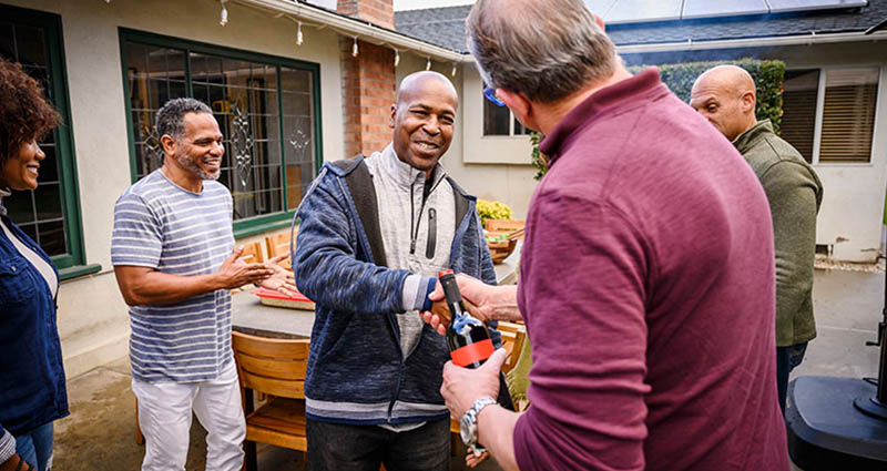  group of four people engaged in a friendly conversation outdoors, with one person handing something to another. 