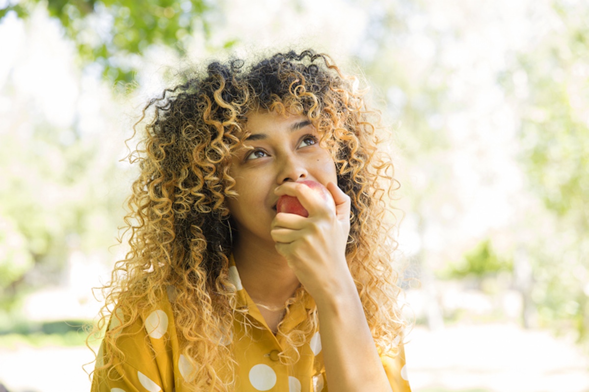 Smiling woman outdoors eating an apple