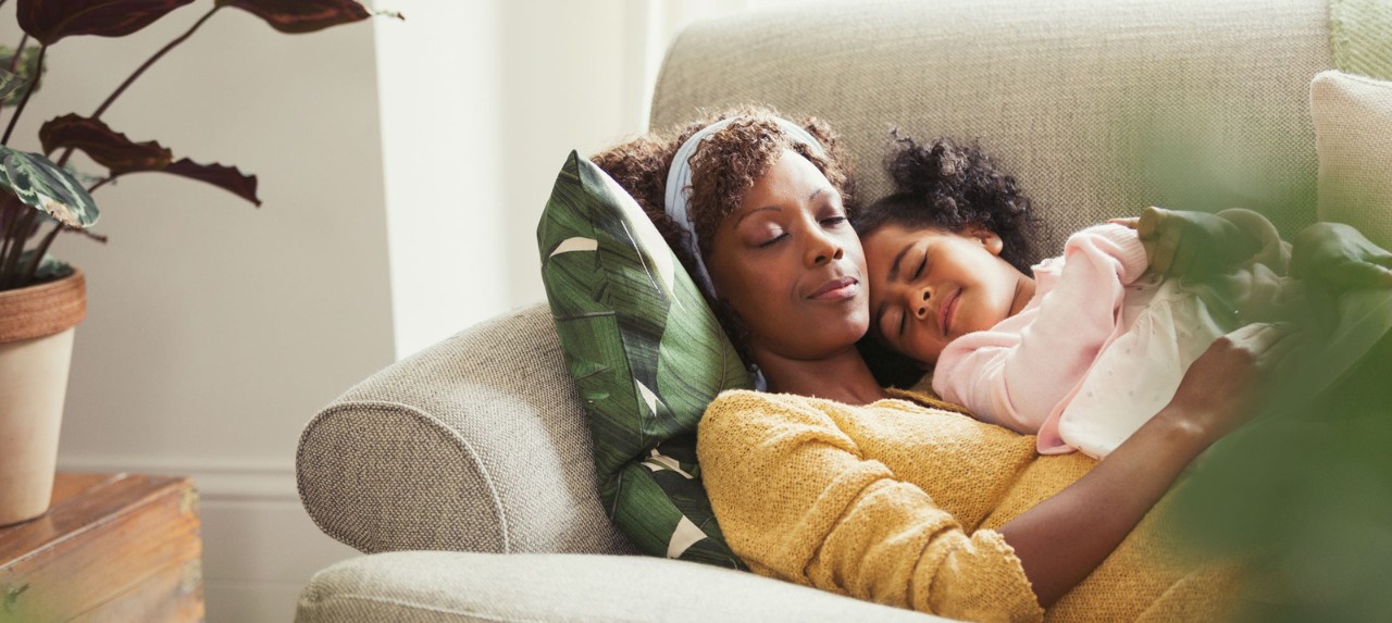 A woman and a young girl cuddling together on a couch, both appearing relaxed and content. 