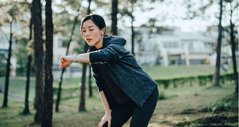 A woman in a black hoodie and leggings exercising outdoors, extending her arm in a focused motion