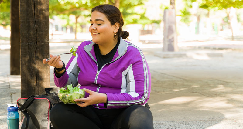 A woman sitting outside while eating a salad