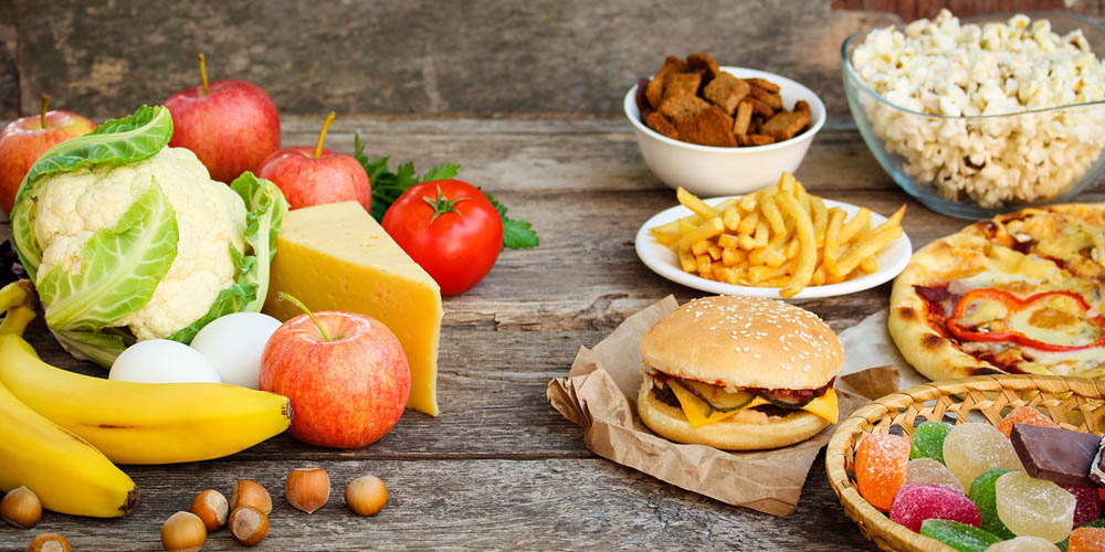Contrast of healthy foods like fruits and vegetables on the left and unhealthy fast foods like burgers, fries, and candy on the right