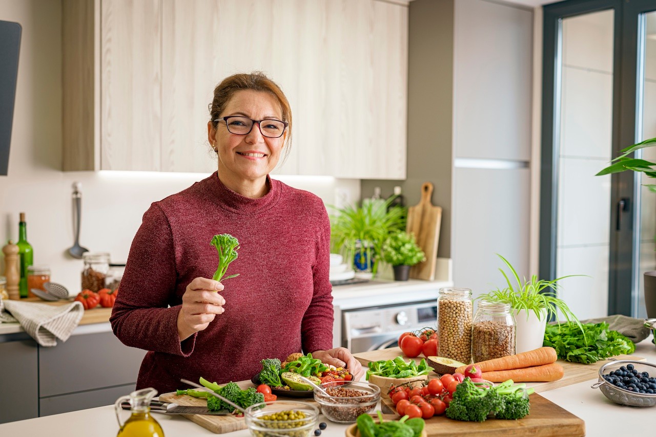 Portrait of a mature Hispanic woman preparing healthy vegan salad plate in domestic kitchen. Healthy eating and dieting concept. High resolution 42Mp indoors digital capture taken with SONY A7rII and Zeiss Batis 40mm F2.0 CF lens