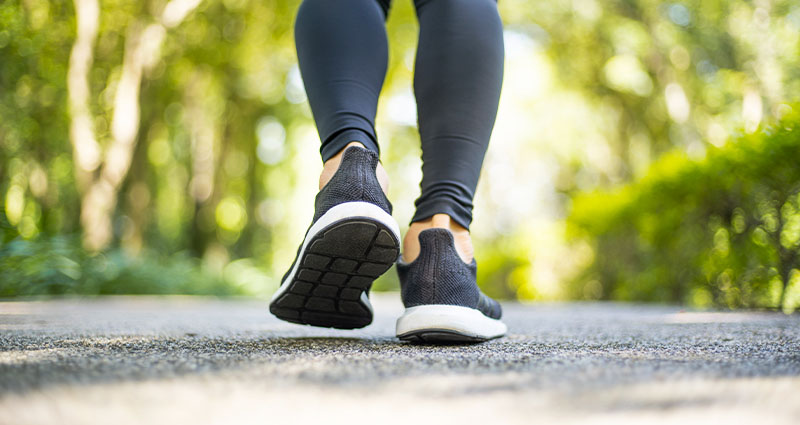 A close-up view of a person walking on a path, showcasing their athletic shoes and fitted leggings