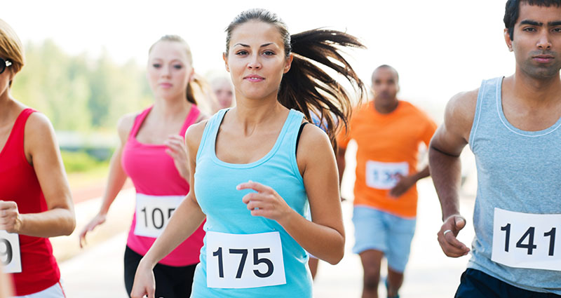 A group of runners participating in a race, with a focus on a woman in a turquoise top wearing a race number 