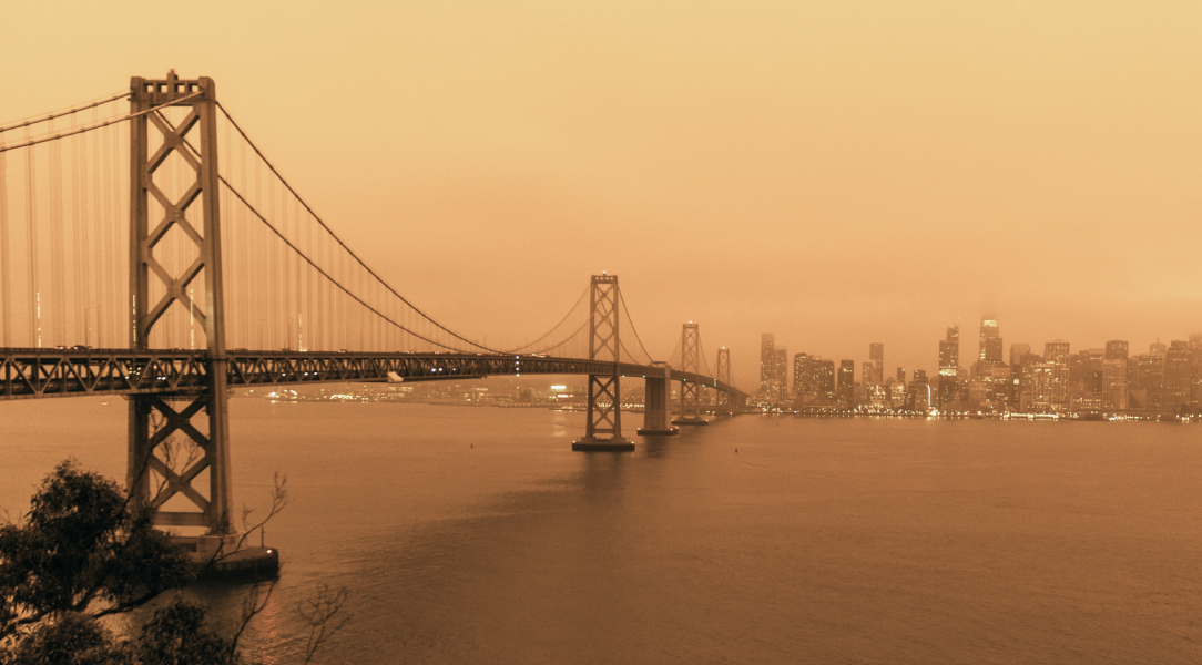 A sepia-toned image of the Bay Bridge with a city skyline in the background