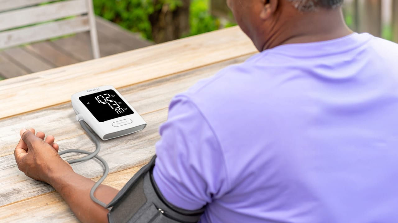 Person using a digital blood pressure monitor with an arm cuff, showing a reading of 102/75 mmHg.