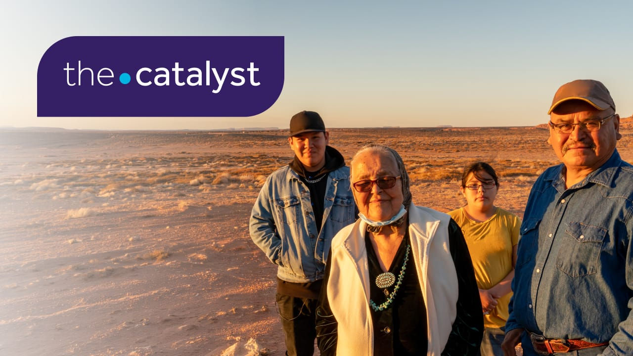 Four people standing in a sunlit desert landscape at sunset, with The Catalyst logo in the upper-left corner.