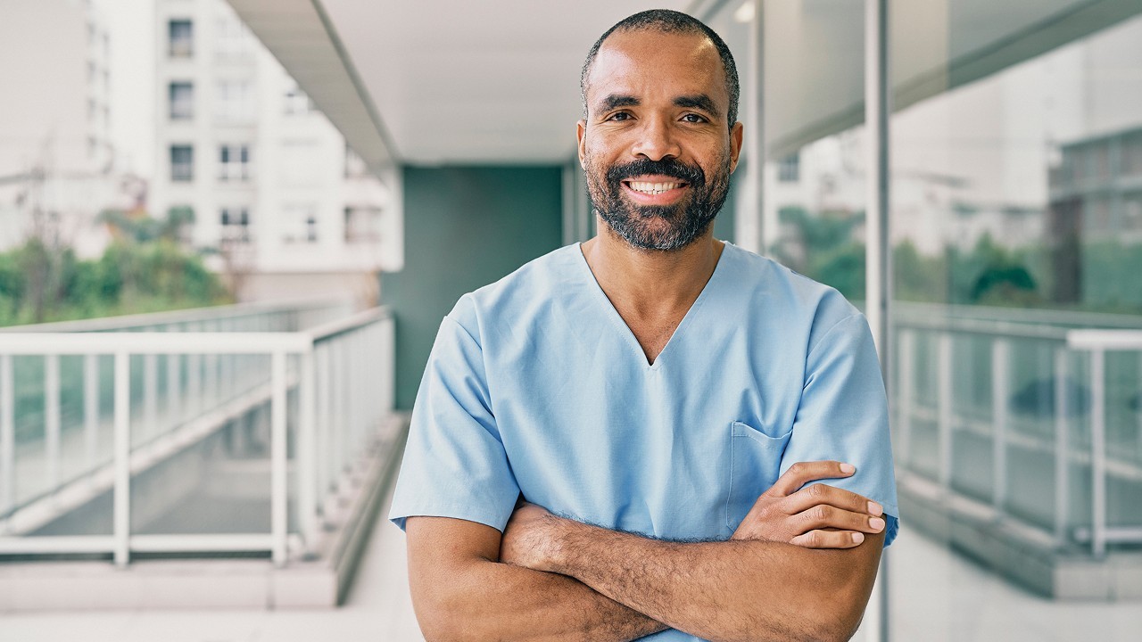 Medical professional standing in hallway with arms crossed and smiling at camera