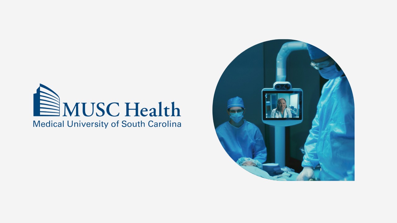 Surgeons operating while a doctor appears on a monitor