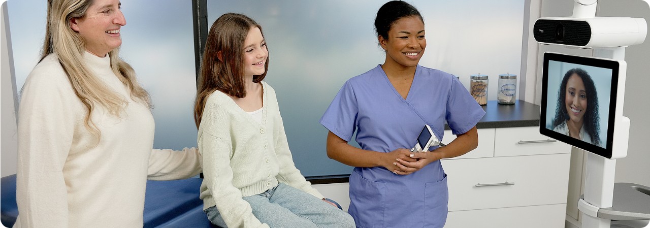 Virtual nurse interacting with a patient and nurse via video monitor in a hospital room.