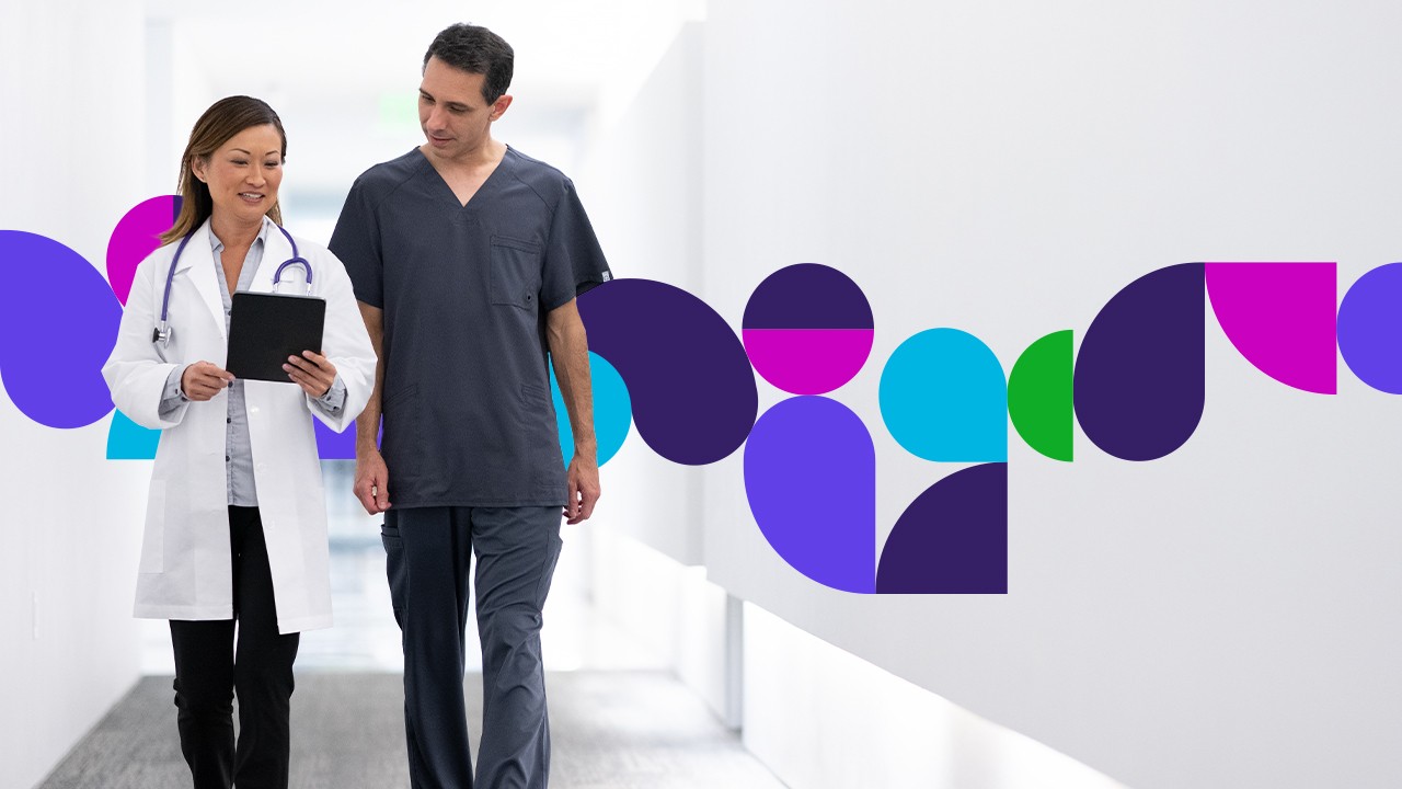 Two medical professionals walking down a hall looking at a tablet