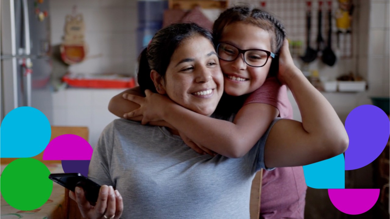 Woman holding cell phone with girl wrapping arms around her from behind