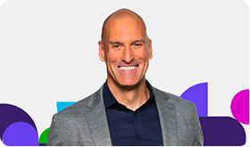 Brian Serfass wearing a gray blazer over a dark shirt with a vibrant background featuring purple, blue, green, and pink shapes.