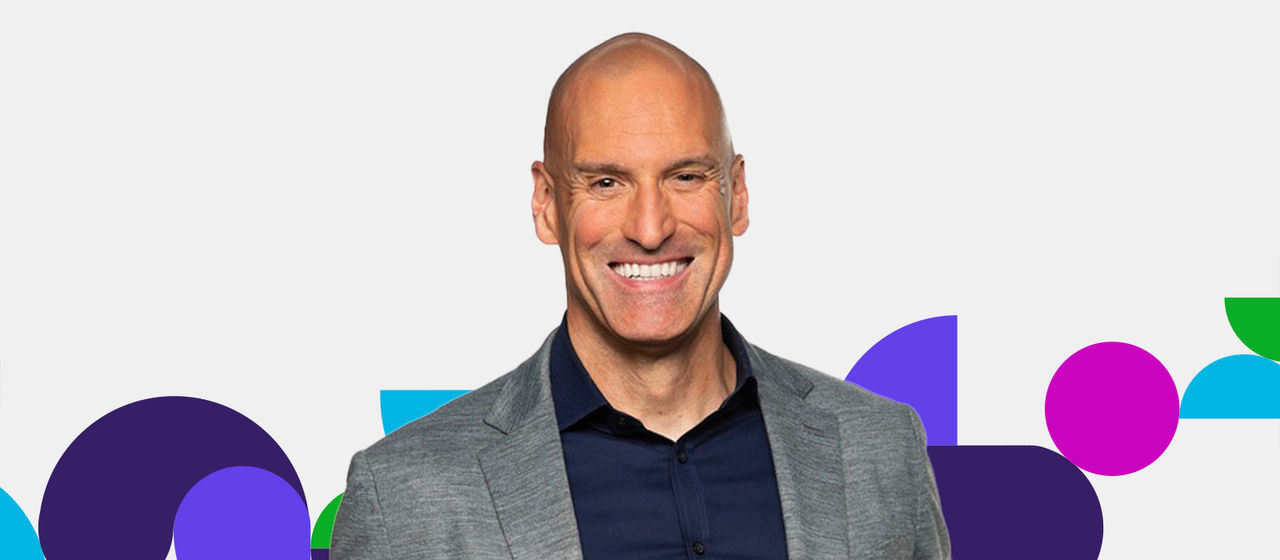 Brian Serfass wearing a gray blazer over a dark shirt with a vibrant background featuring purple, blue, green, and pink shapes.